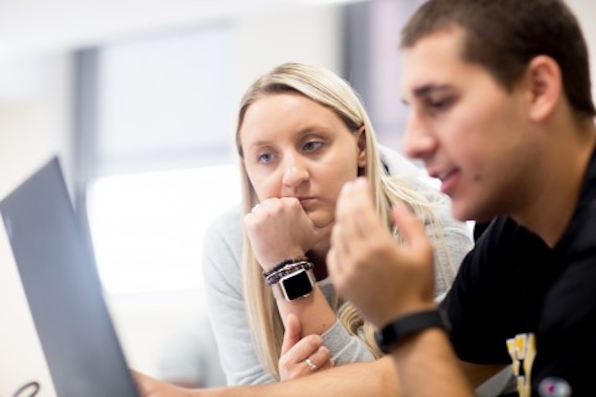 woman looking over shoulder of man at laptop