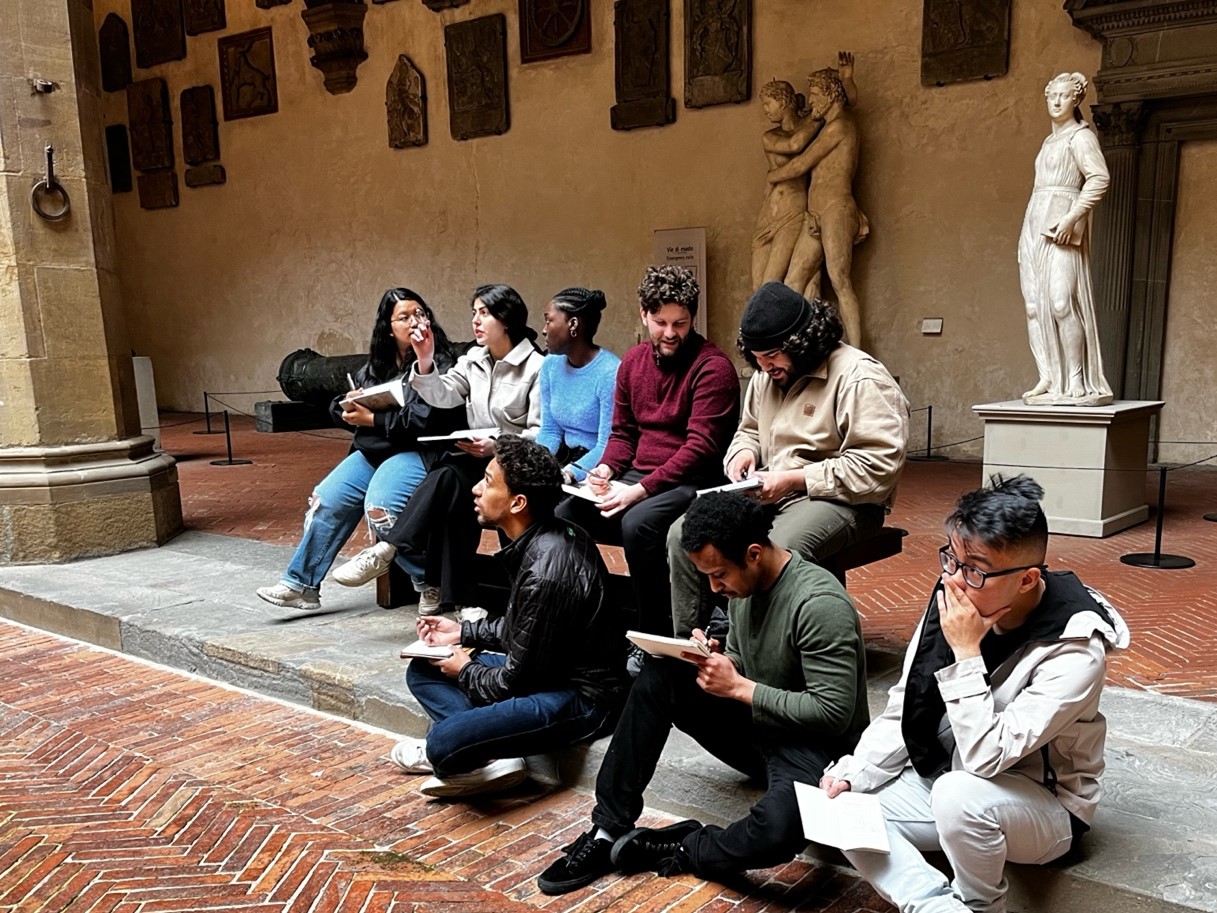 Architecture students sitting outside of a museum in Italy and taking notes or drawing on pads