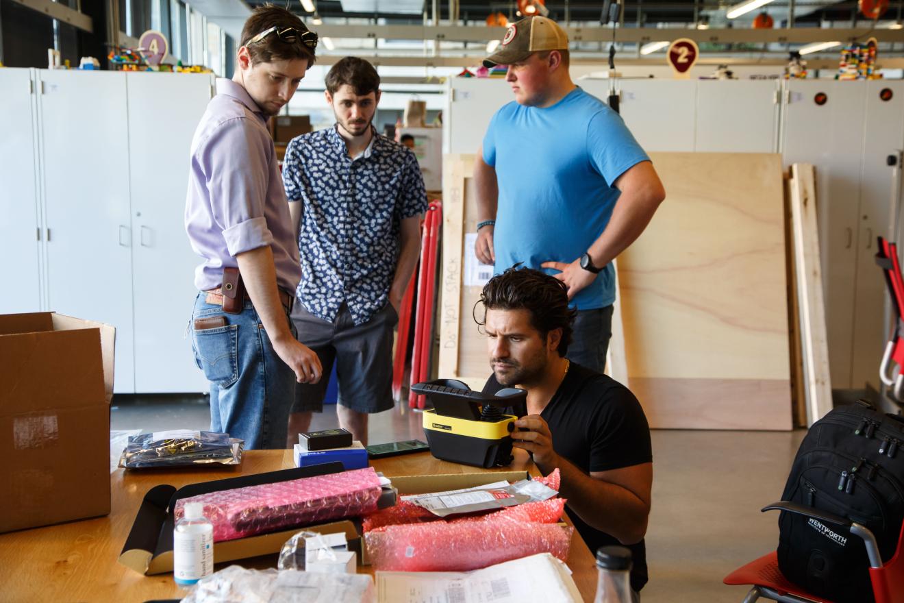 students and alum working with robot