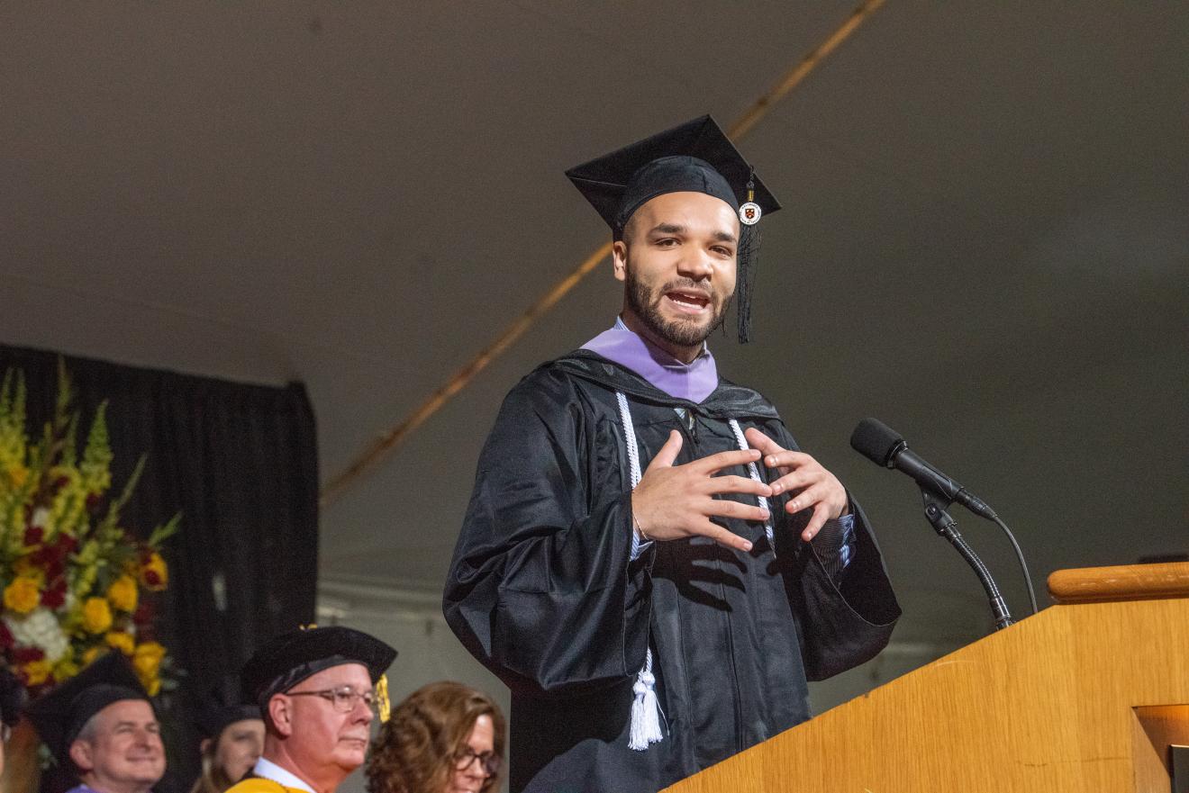 man speaking at a podium in graduation robe