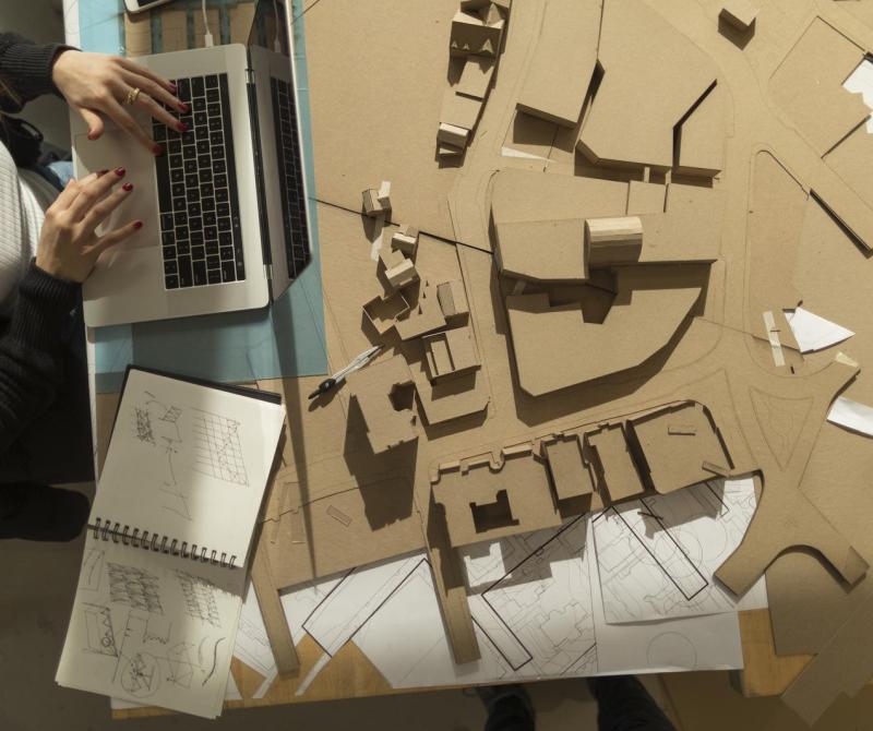 Architectural models and a student working on design files on a laptop