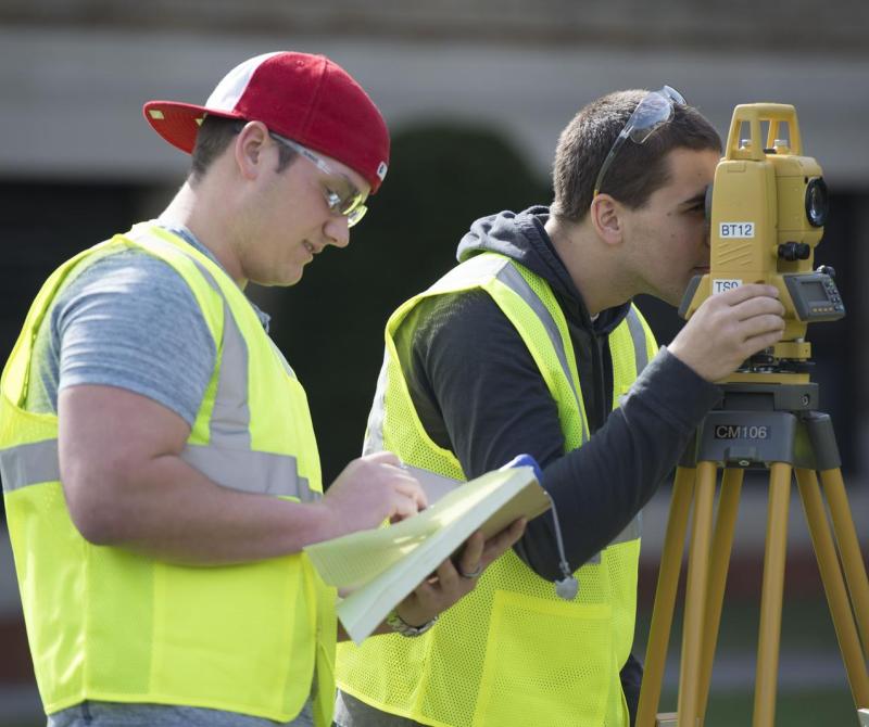 Two students wearing bright vests practice surveying in Boston