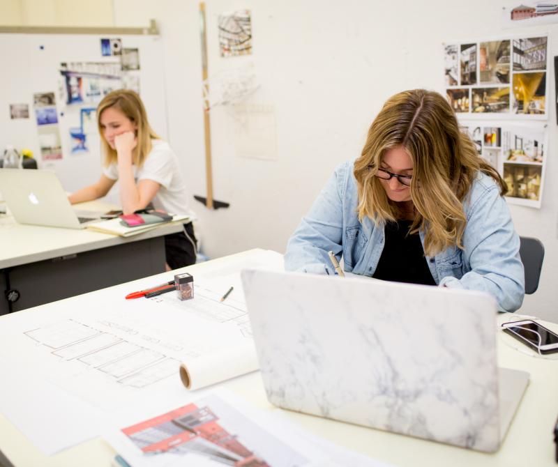 Two students work on laptops in the interior design lab