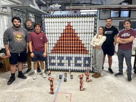 students pose in front of an image created by stacking cans strategically