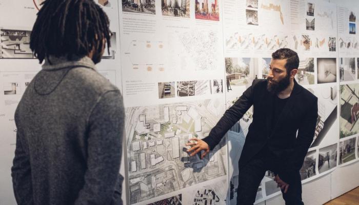 Two architecture students discuss a design pinned to the wall