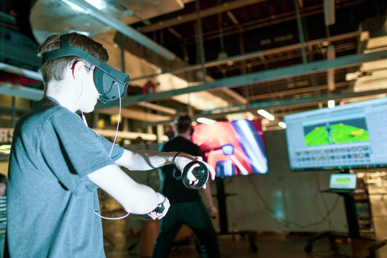 Two male students test out VR headsets in front of televisions