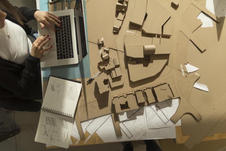 Architectural models and a student working on design files on a laptop