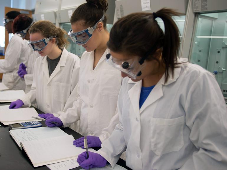 Women in lab gear working on class notes.