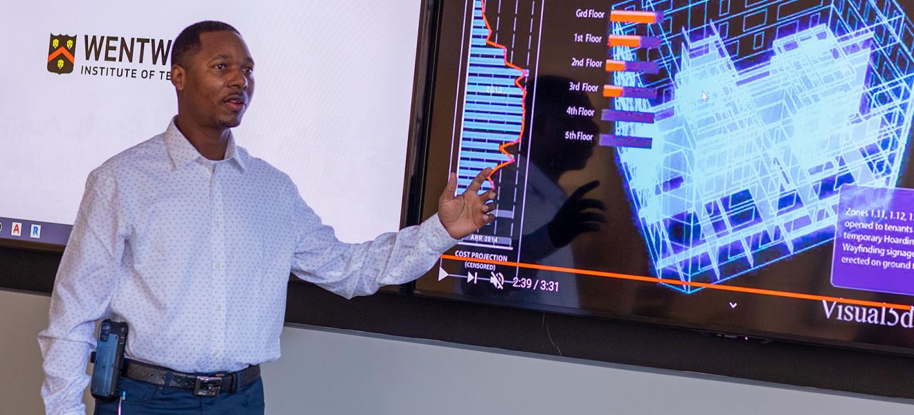 A man points at a projection in front of a classroom. 