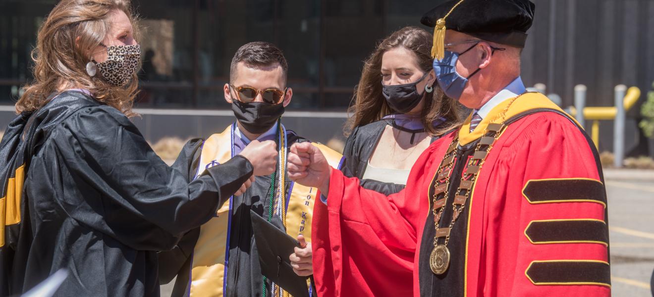 man wearing graduation robe offers a fist bump to a student