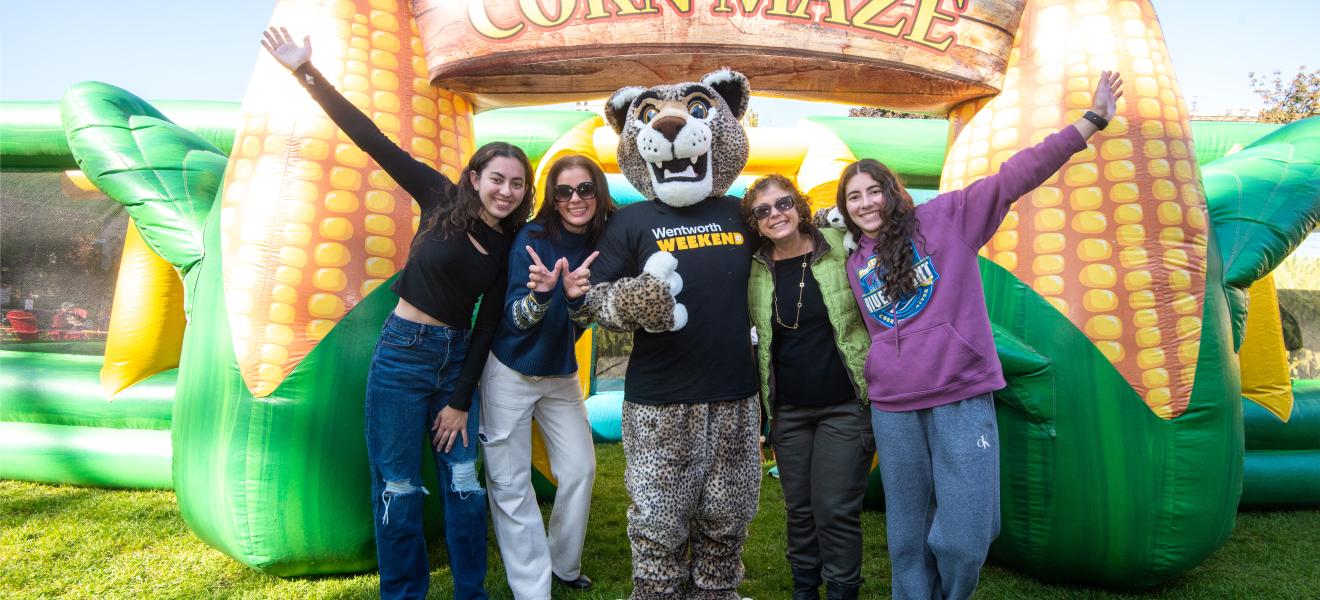 four people and a leopard mascot pose in front of an inflatable corn maze