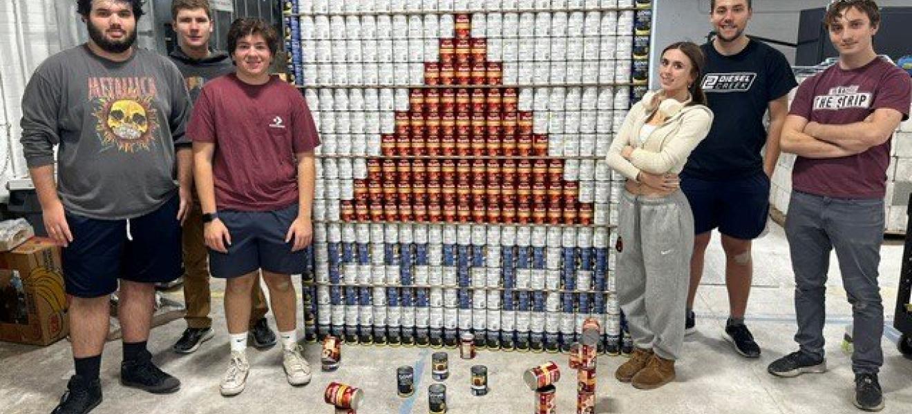 students pose in front of an image created by stacking cans strategically